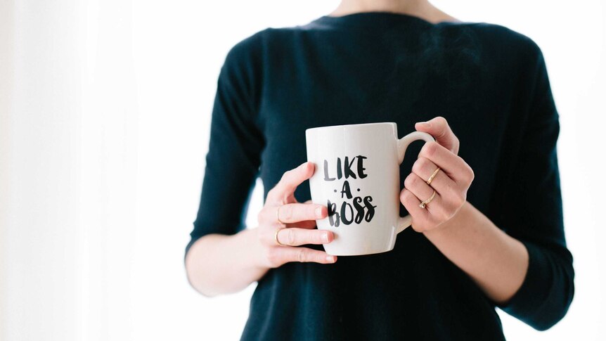 A woman wearing a black jumper holds a mug that reads "Like a boss".