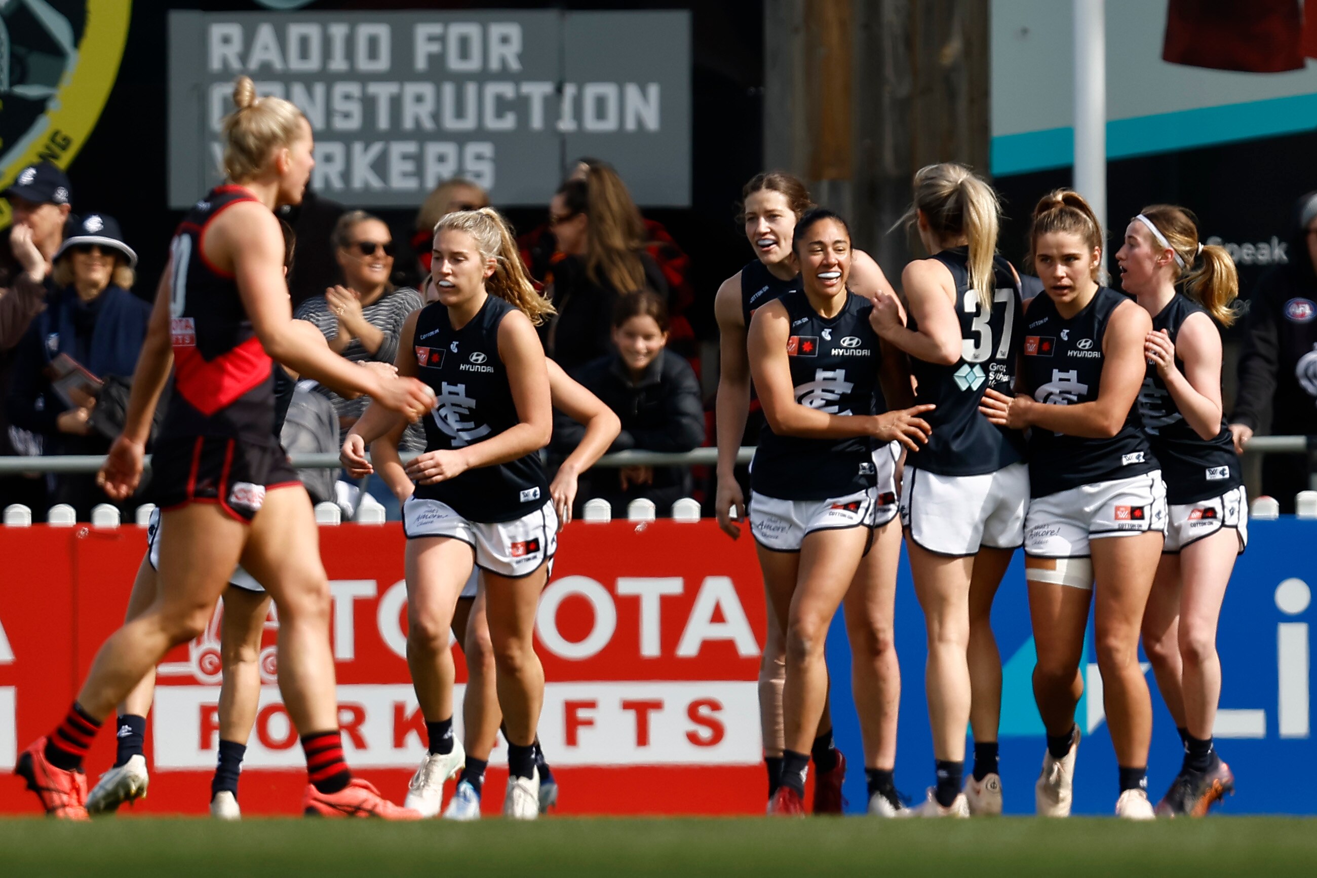 A grinning Darcy Vescio walks back after kicking a goal as their Carlton teammates congratulate them.