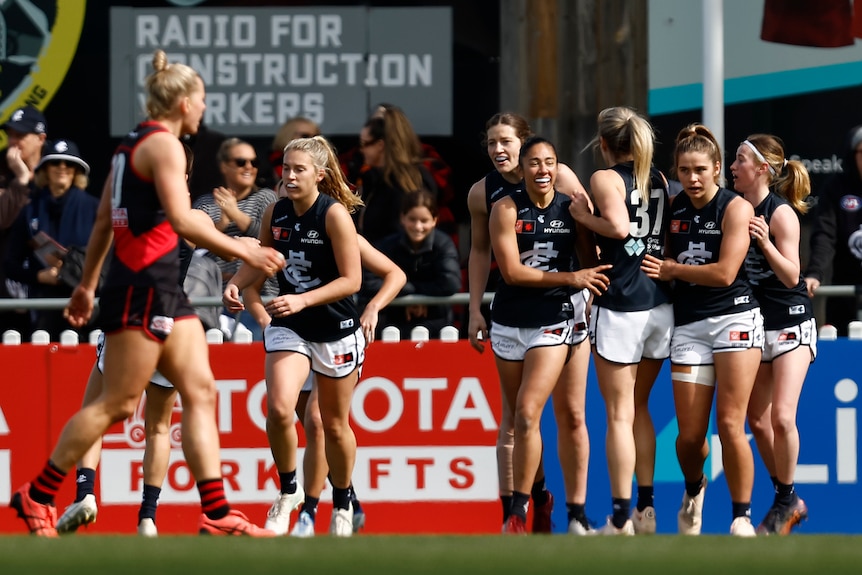 A grinning Darcy Vescio walks back after kicking a goal as their Carlton teammates congratulate them.