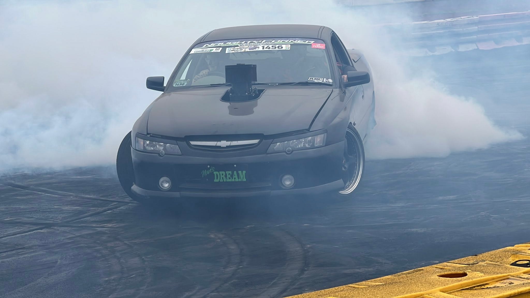 A woman drives a black ute as grey smoke appears at the back of the vehicle