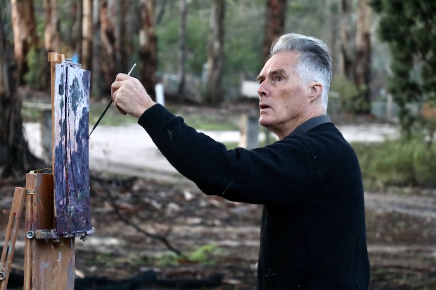 Warwick Fuller paints outside on a canvas.