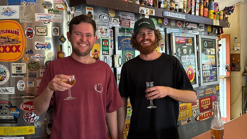 Two young publicans smile behind an eclectic pub bar