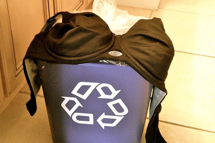 A black  bra sitting on top of a recycling bin.