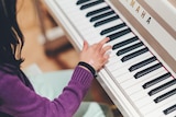 A young girl picks out a note on a piano keyboard. 