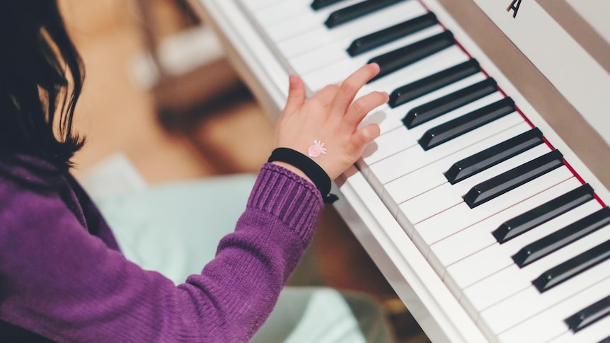 A young girl picks out a note on a piano keyboard. 