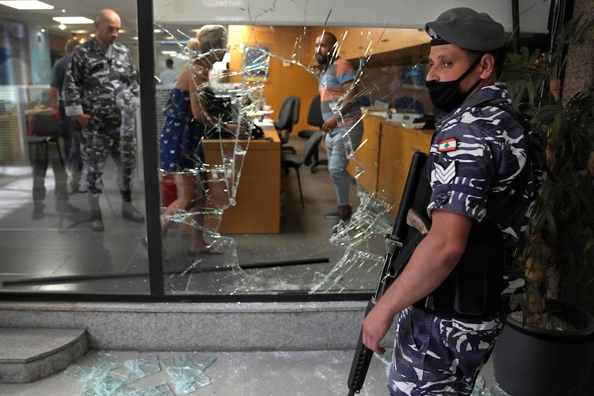 A Lebanese policeman stands guard next to a bank window.