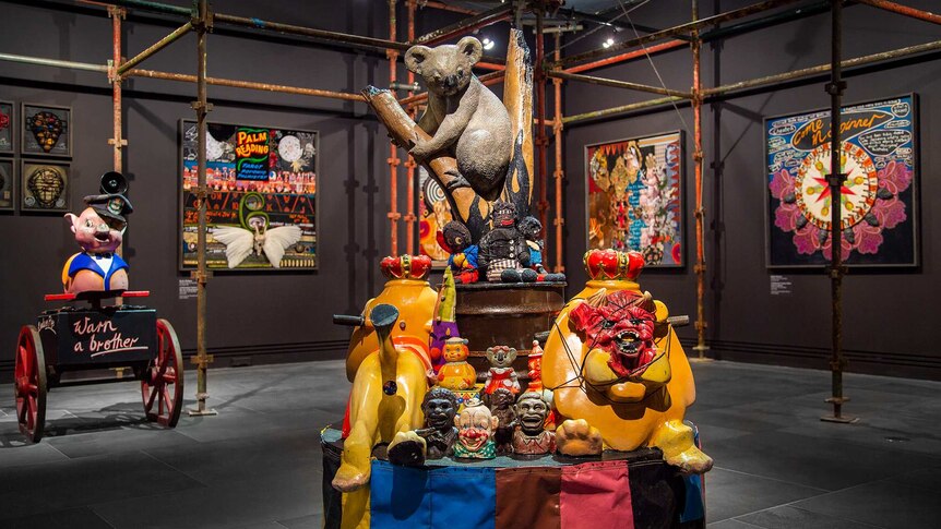 Gallery space with sculpture in foreground made from vintage carnival rides, racist kitsch objects and a large model koala.