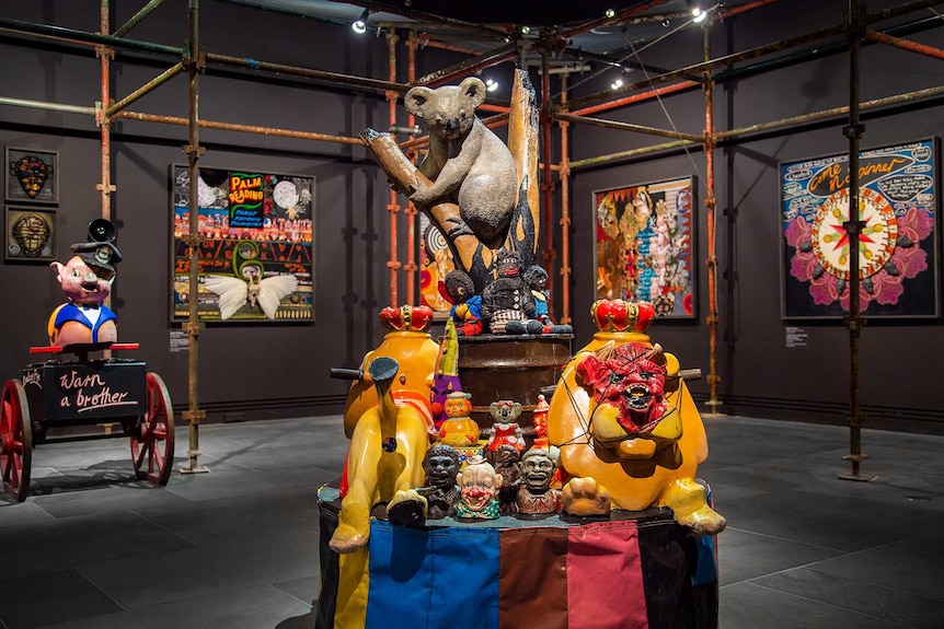 Gallery space with sculpture in foreground made from vintage carnival rides, racist kitsch objects and a large model koala.