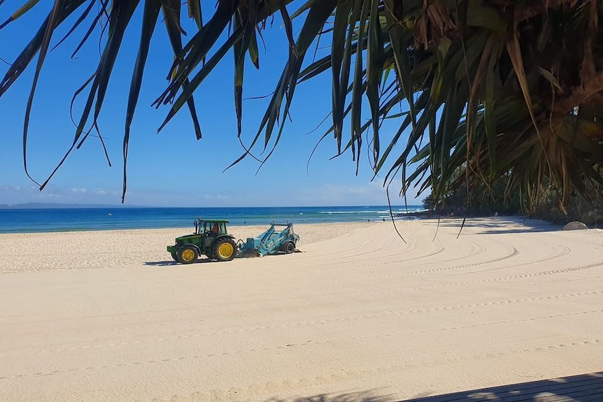 A tractor driving on the sand cleaning the beach with a trailer