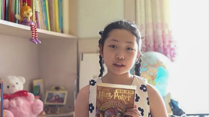 A young Asian girl holds a copy of Harry Potter in her bedroom