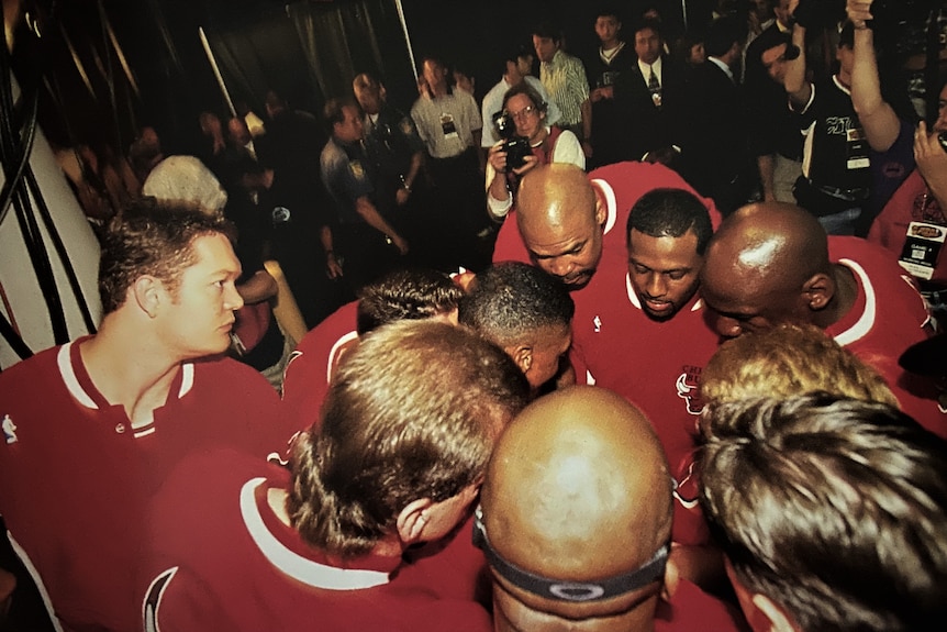 A group of male basketball players in red Chicago Bulls sweat shirts huddle