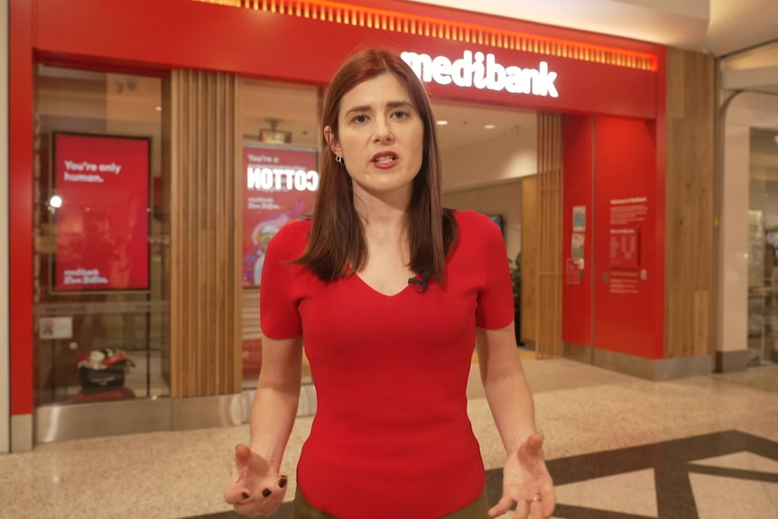 Woman in red top standing in front of Medibank shopfront in a shopping centre.