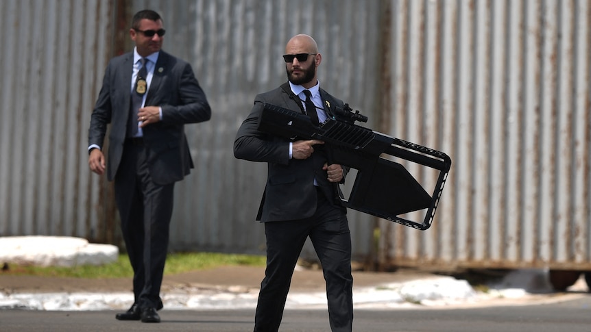 A security agent in a suit with an enormous black anti-drone rifle