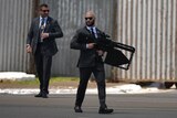 A security agent in a suit with an enormous black anti-drone rifle