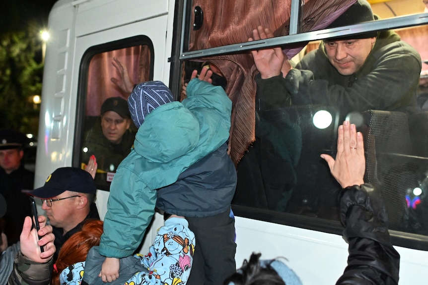 People bid farewell to reservists in civilian clothes as the sit aboard a bus to be transported.