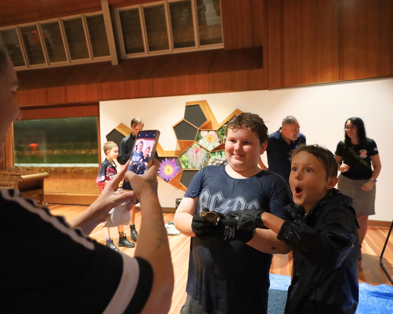 Duas crianças seguram um grande sapo-cururu enquanto um pai tira fotos deles.