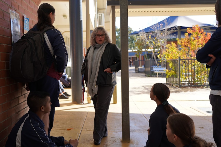 A woman stands talking to a group of teenage school students.