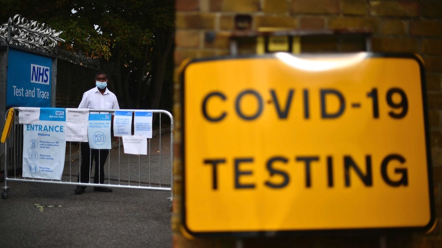 A member of staff stands at the entrance to a coronavirus testing centre as a yellow sign says: "COVID-19 testing."