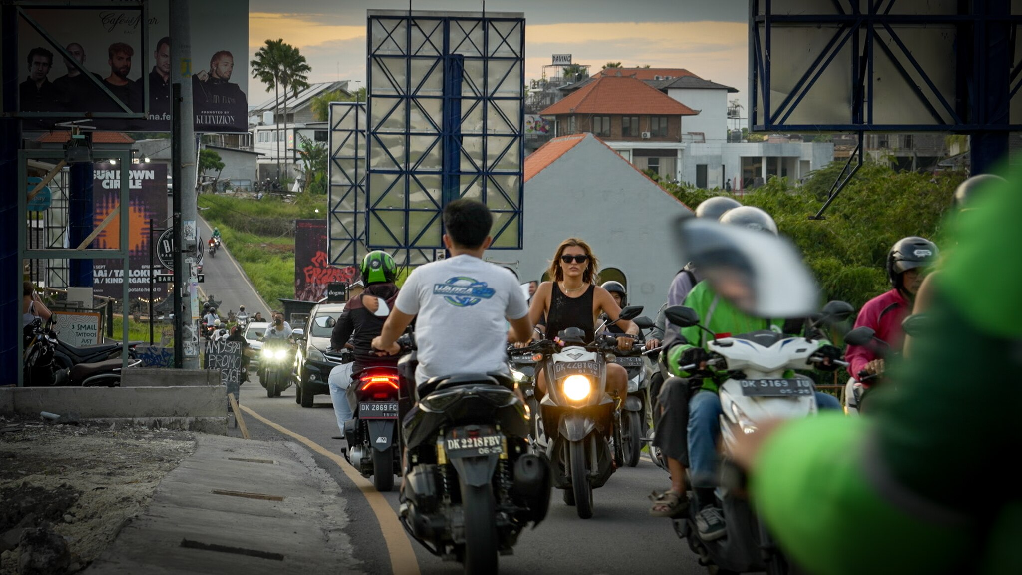 A young blonde woman rides a scooter down a busy road