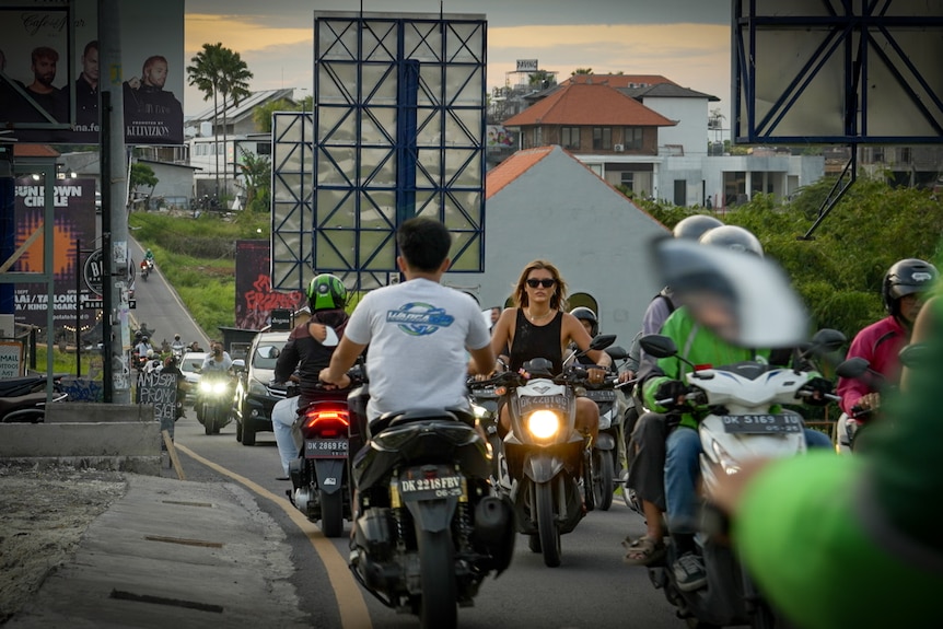 Wanita pirang muda mengendarai sepeda motor di jalan yang sibuk