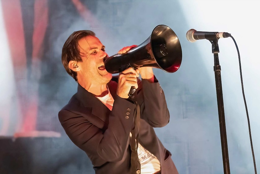 Phil Jamieson of Grinspoon sings through a megaphone into a microphone on stage