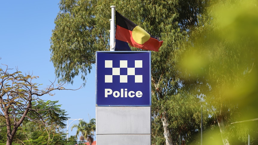 A police sign surrounded by trees, with the Aboriginal flag behind it