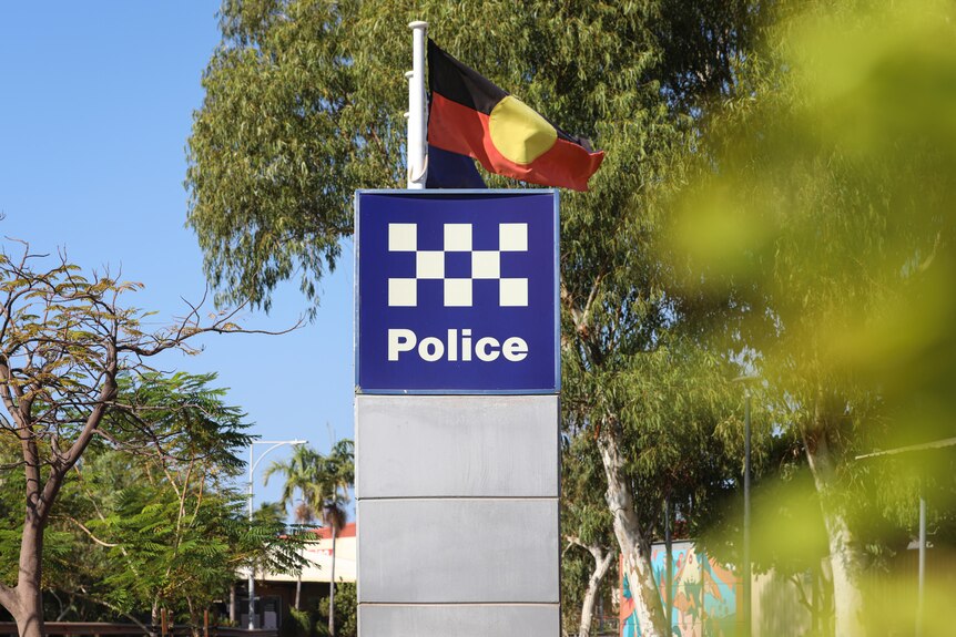 A police sign surrounded by trees, with the Aboriginal flag behind it.