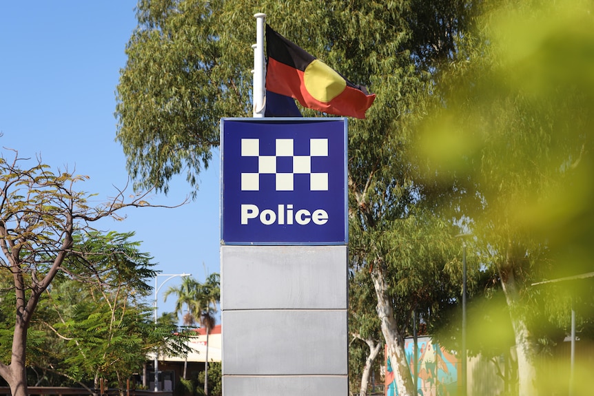 A police sign surrounded by trees, with the Aboriginal flag behind it.