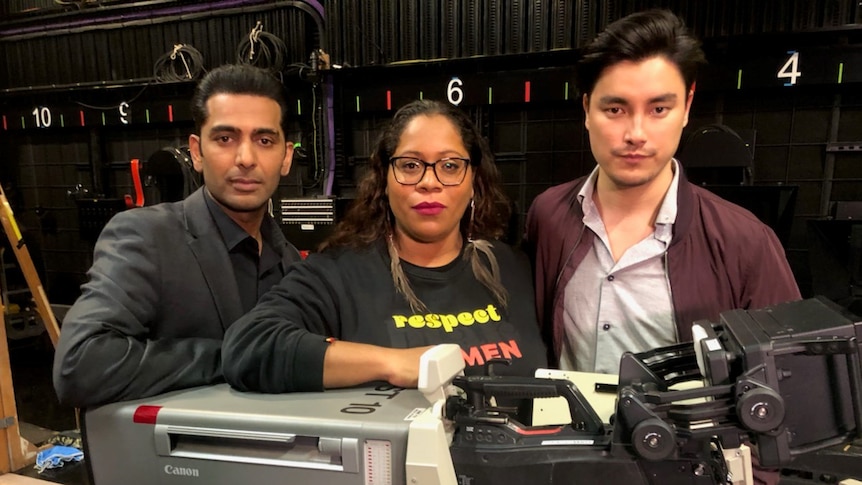 Three people stand behind a TV camera.