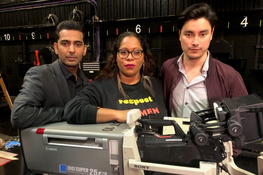 Three people stand behind a TV camera.