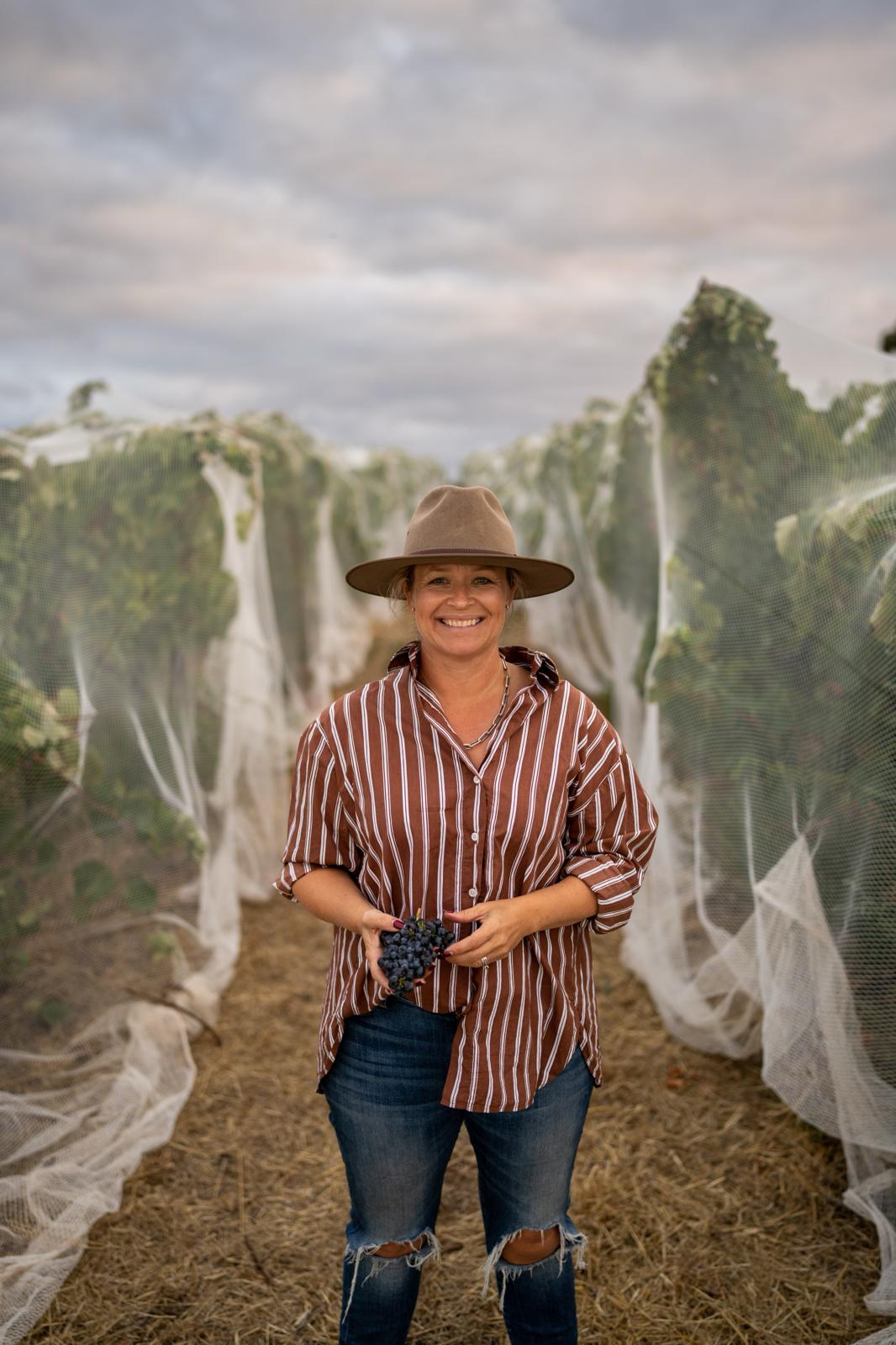 a woman stands in between rows of winegrapes draped in white nets
