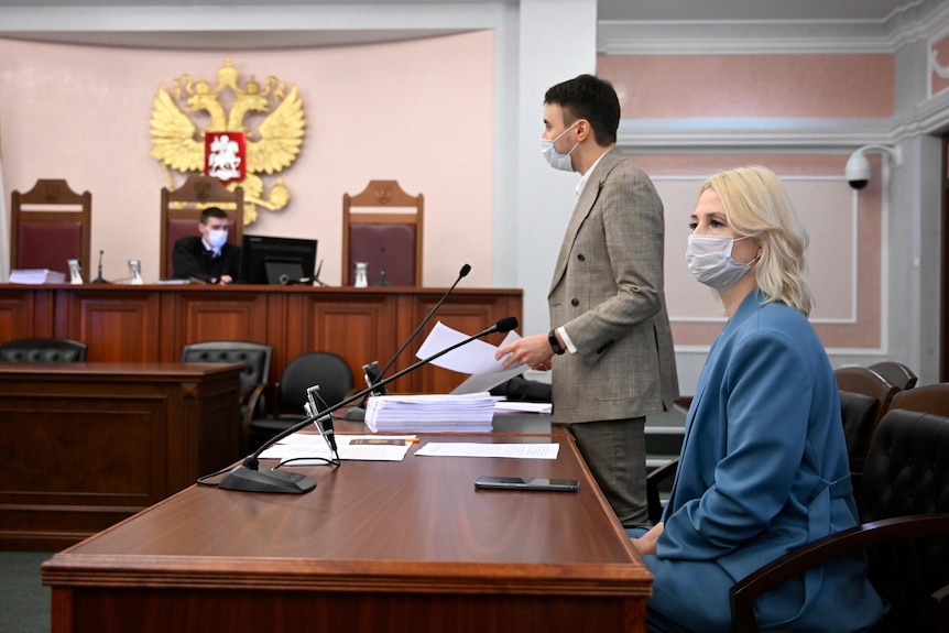 A woman in a blue suit sits in Russian court room. 