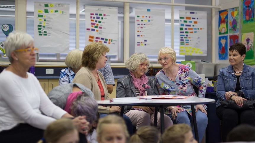 A group of grandparents in a classroom sitting around desks with children
