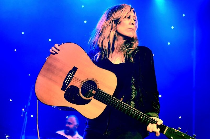 A woman stands on stage holding a guitar.