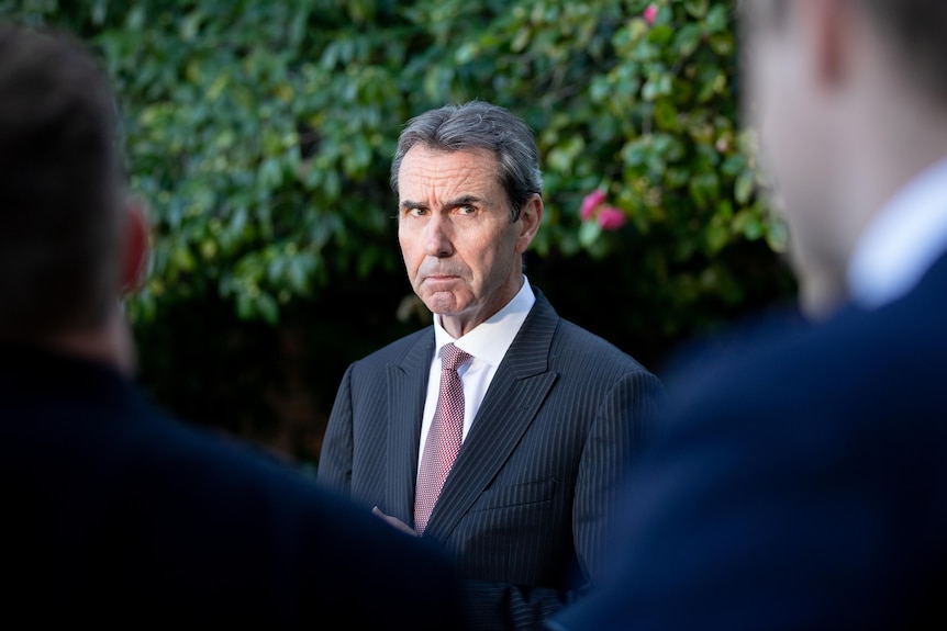 Man in suit with tie looking very serious while talking to group of people.