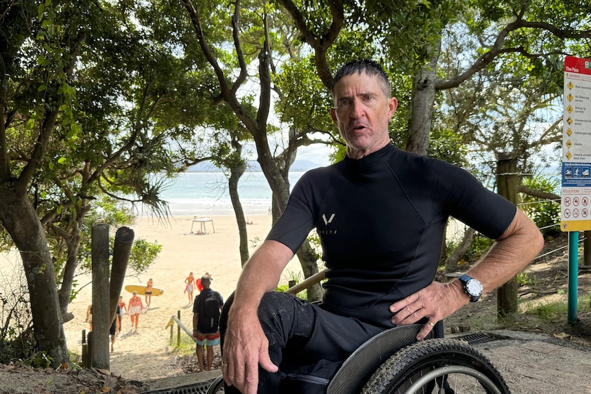 A man in a wheelchair, wearing a wetsuit sits at the top of a steep set of stairs at Byron Bay.