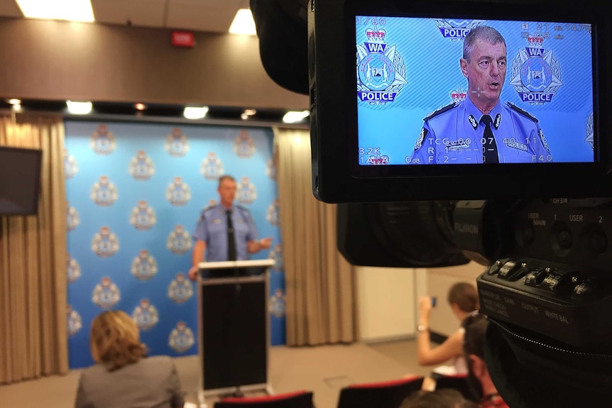 WA Police Commissioner Karl O'Callaghan seen on the viewfinder of a camera as he speaks to reporters in the background.