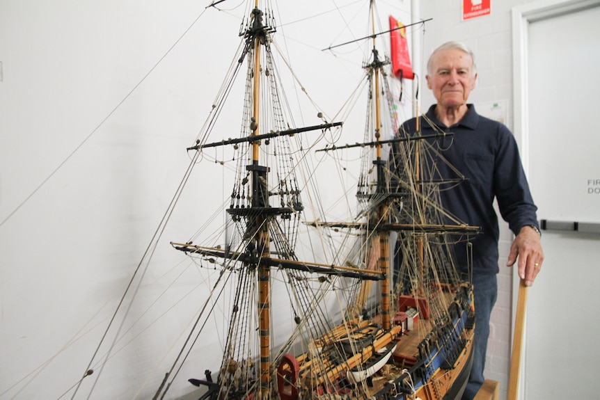 A man stands next to a large tall ship model (over a metre high).
