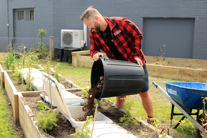 Ryan Aitchison pours a bucket of food waste into a white bin in a garden.