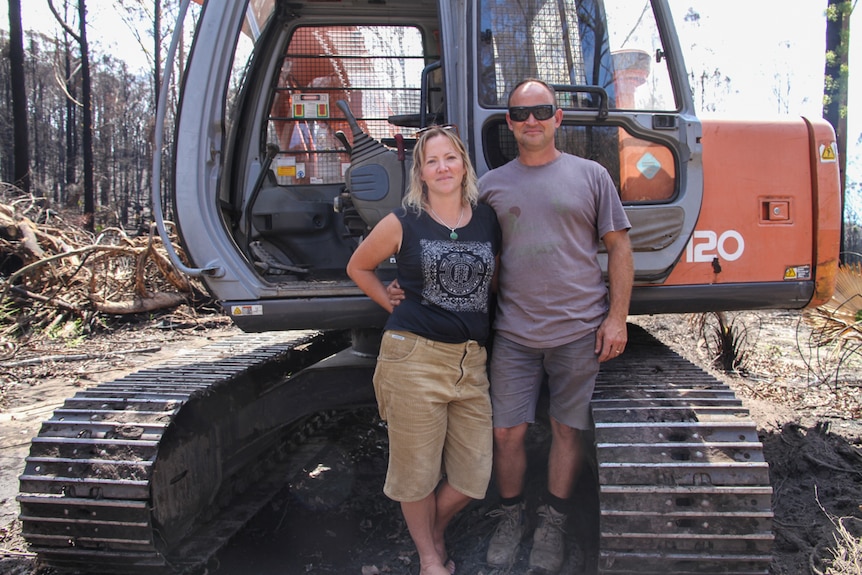 A couple of people stand in front of a large piece of earth moving machinery