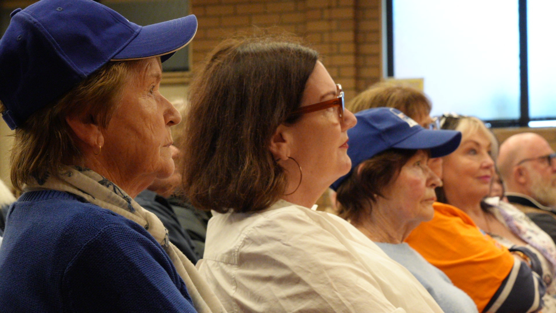 Older women in seats at an event in a community hall.