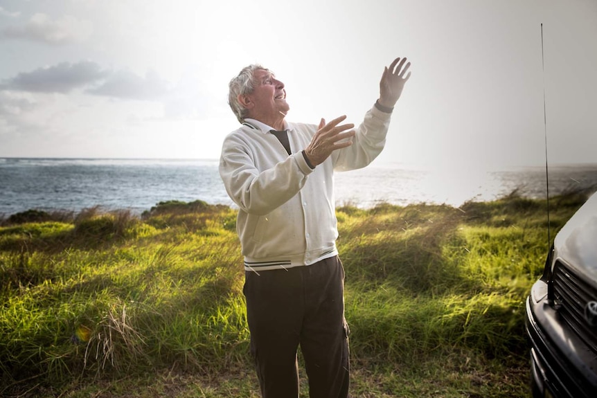 A man with his hands in the air, with the ocean seen behind him.