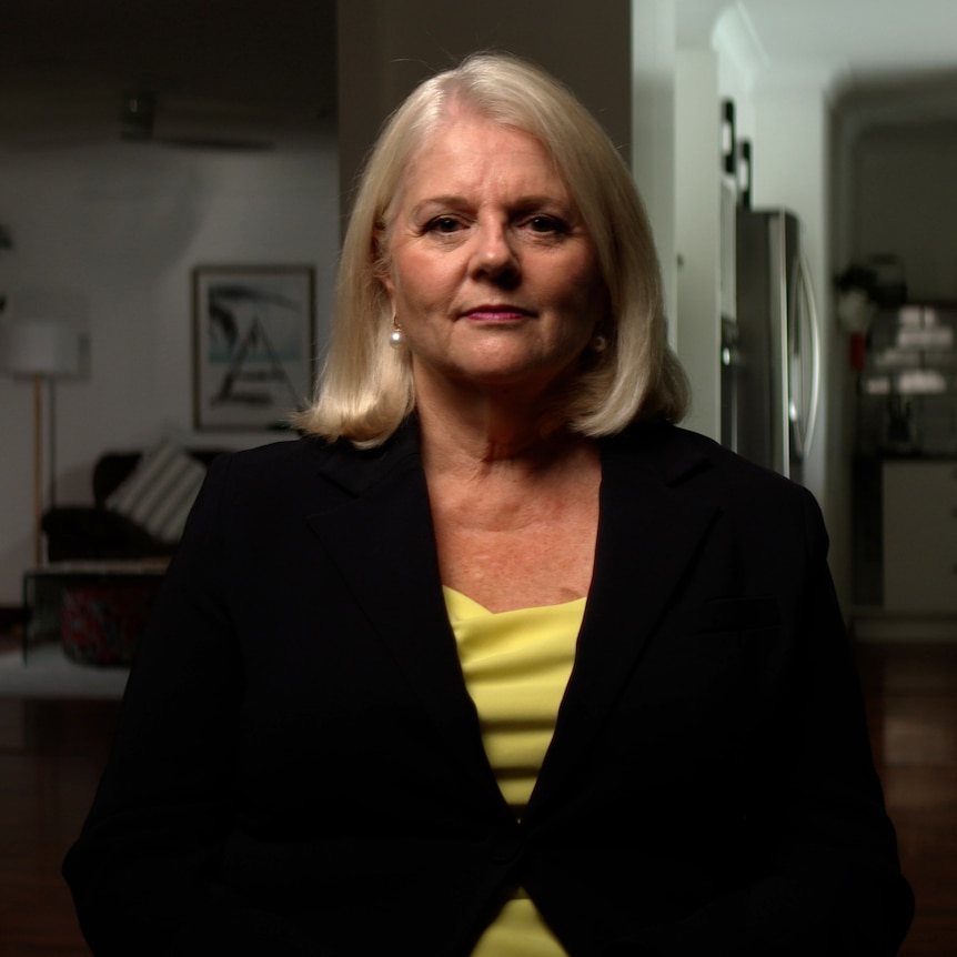 Karen Andrews sits on a chair in a home, looking into camera with a serious expression on her face.