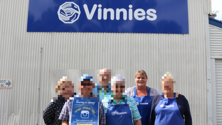 Four people wearing blue aprons in front of a corrugated iron wall with a Vinnies sign on it