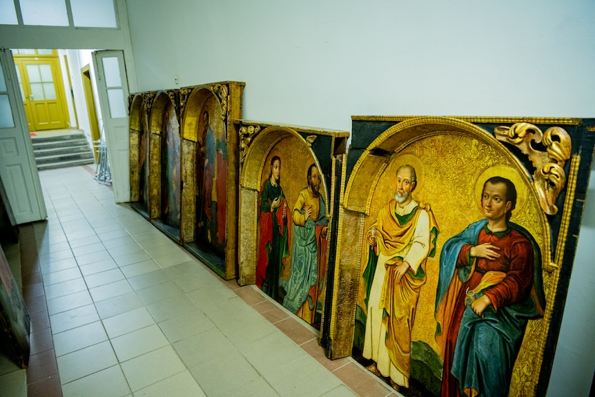 Pieces of old religious art are sitting on the floor and resting against a wall in a hallway.