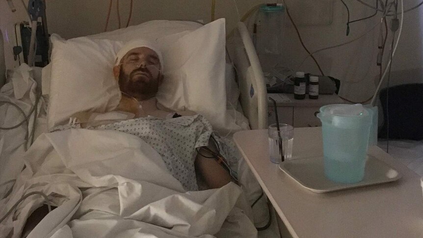 A man with a beard laying down with his eyes closed in a hospital bed