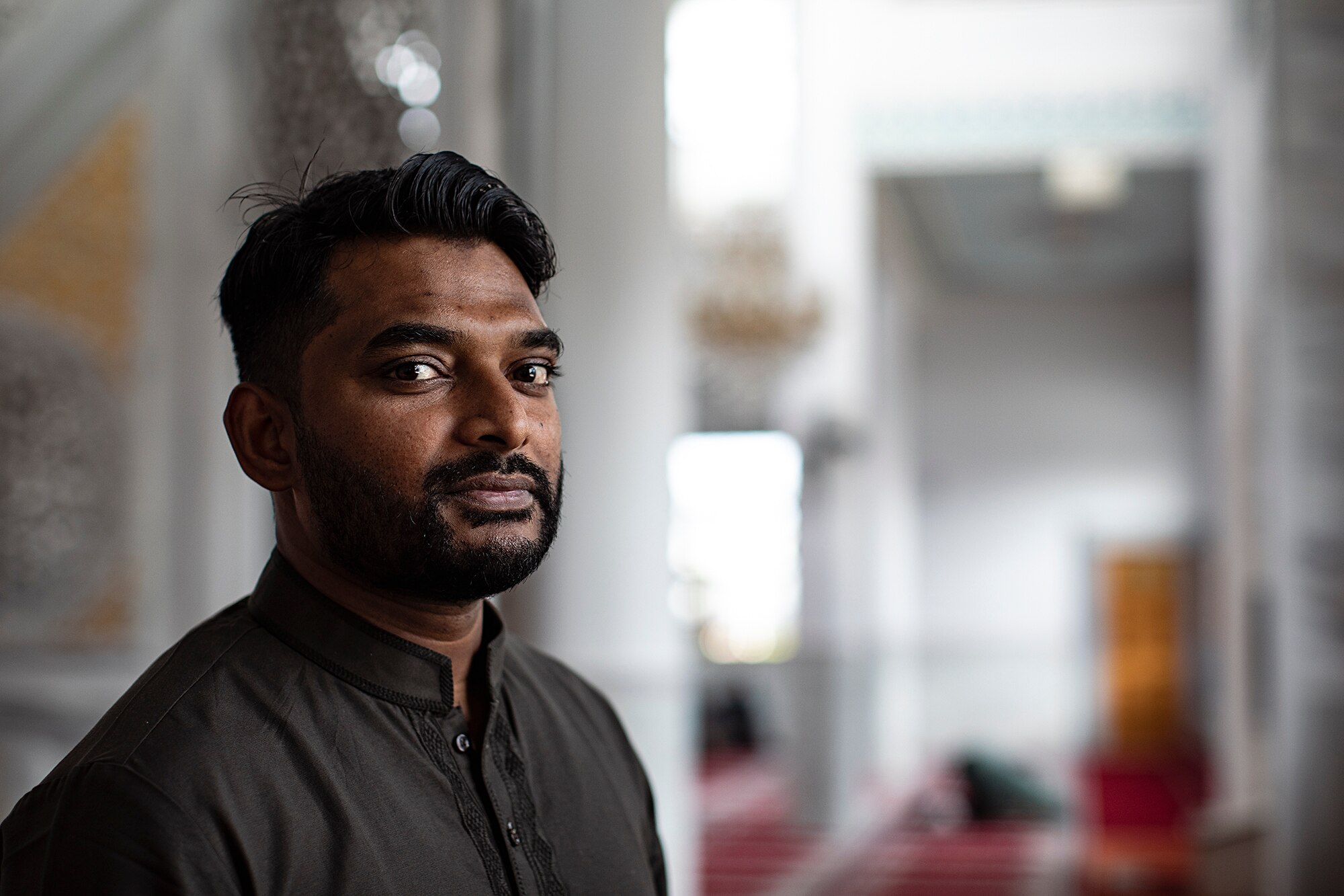 Khaled Shaikh kneels on red carpet inside a mosque during daytime.