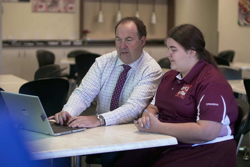 A man types on a laptop as a teenage girl watches the screen.