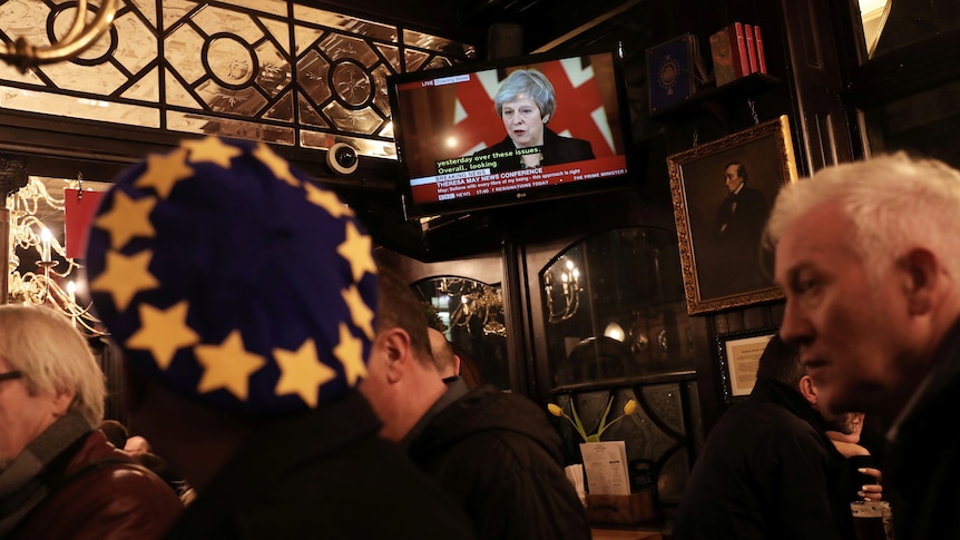 People in a pub watch Theresa May on television