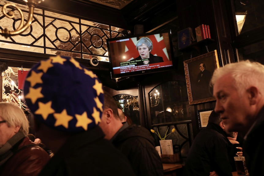 People in a pub watch Theresa May on television